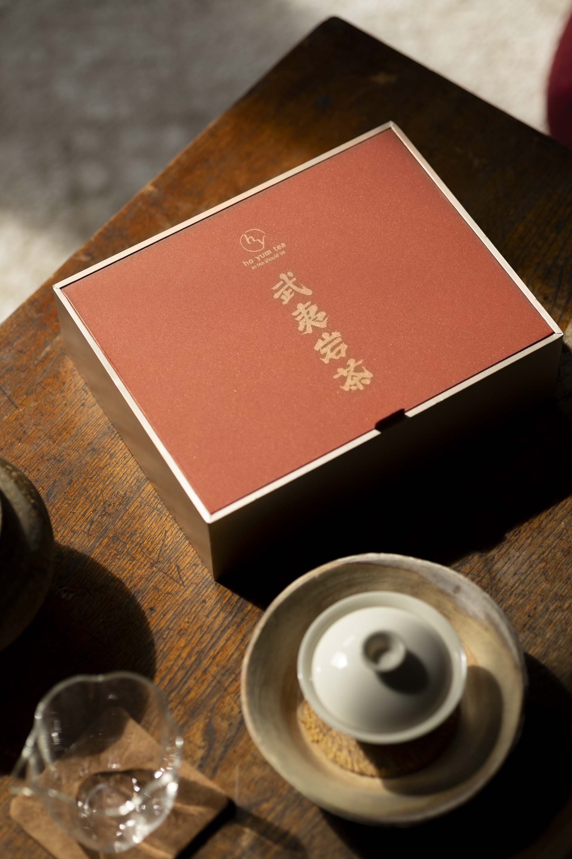 The hyt Wuyi Yancha wulong tea collection gift box on a wooden table beside a white ceramic gaiwan and glass tea pitcher in warm natural light.
