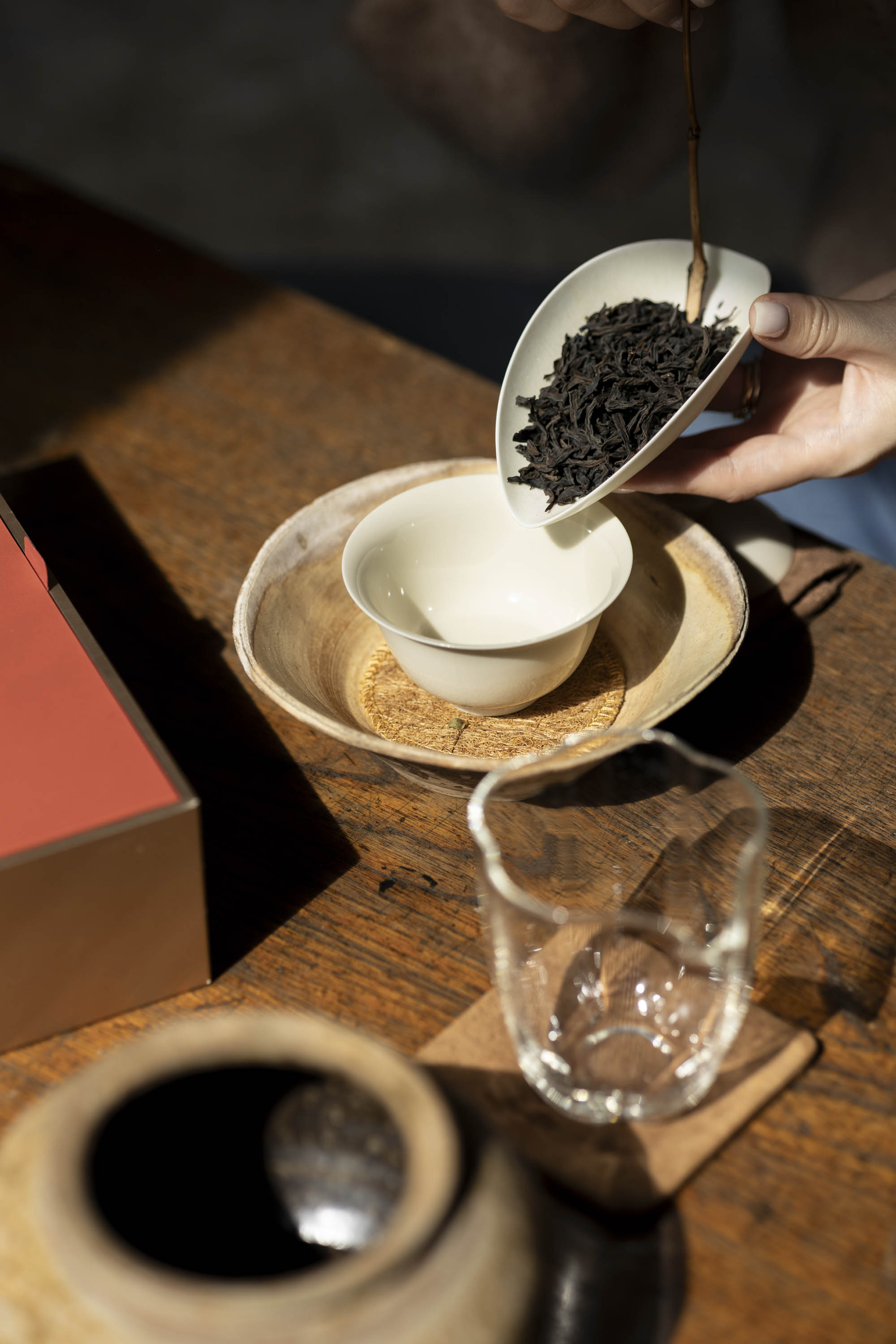dark Wuyi Yancha wulong tea leaves from a scoop into a white ceramic gaiwan