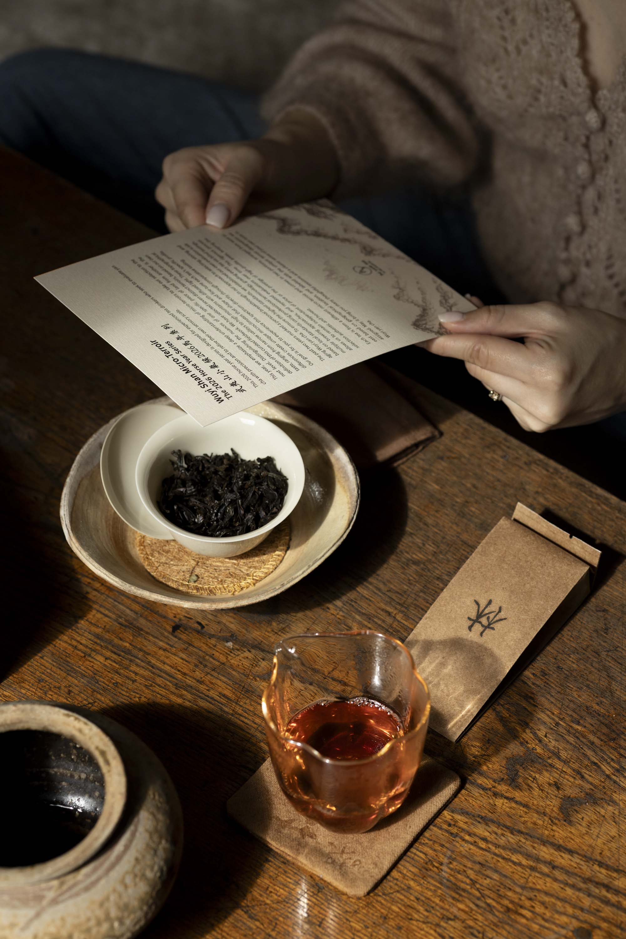 the Wuyi Shan Micro-Terroir 2026 Horse Year Series introduction card over a white gaiwan of dark wulong tea leaves and a glass pitcher of brewed yancha on a wooden table.