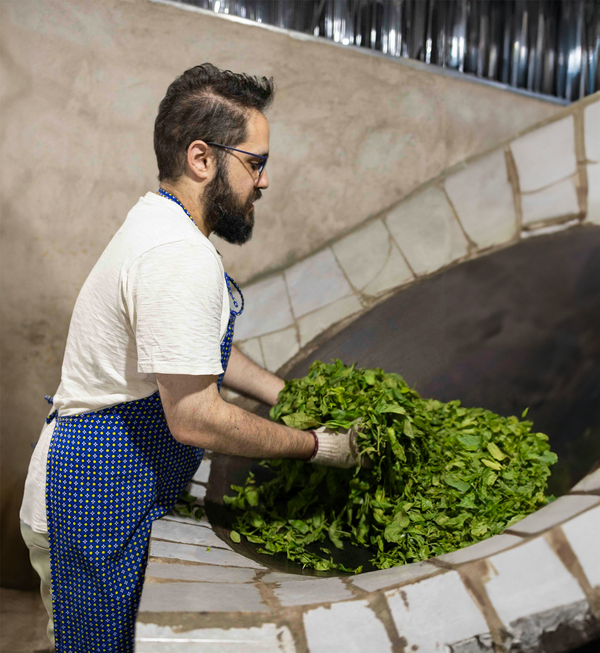 Nadi Biran hand-firing (shaqing) fresh tea leaves in a hot wok at a tea factory in Yongde, Lincang, Yunnan