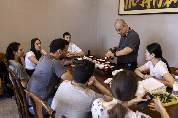 A tea master serving a group seated around a long tasting table