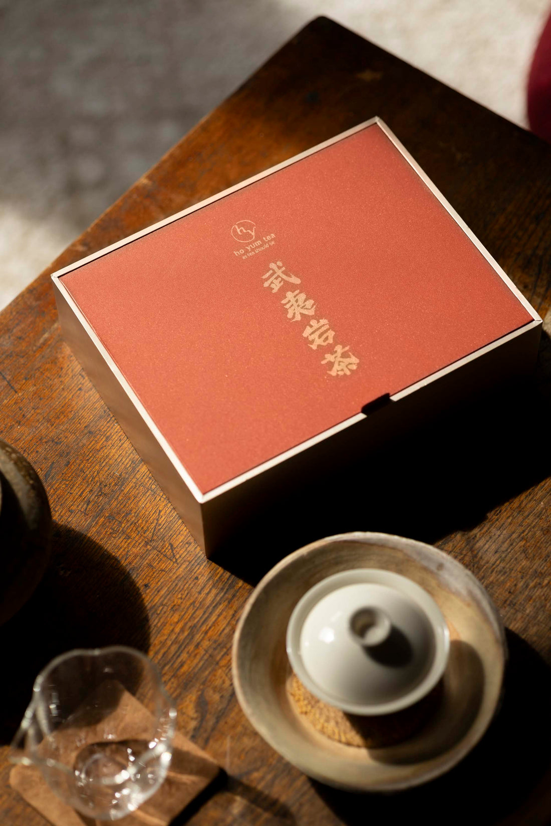 The hyt Wuyi Yancha wulong tea collection gift box on a wooden table beside a white ceramic gaiwan and glass tea pitcher in warm natural light.