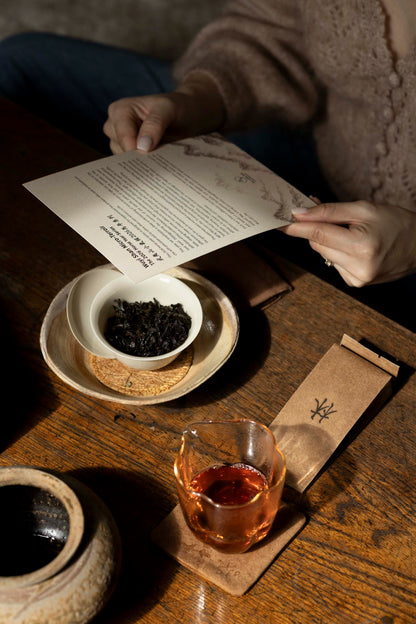 the Wuyi Shan Micro-Terroir 2026 Horse Year Series introduction card over a white gaiwan of dark wulong tea leaves and a glass pitcher of brewed yancha on a wooden table.